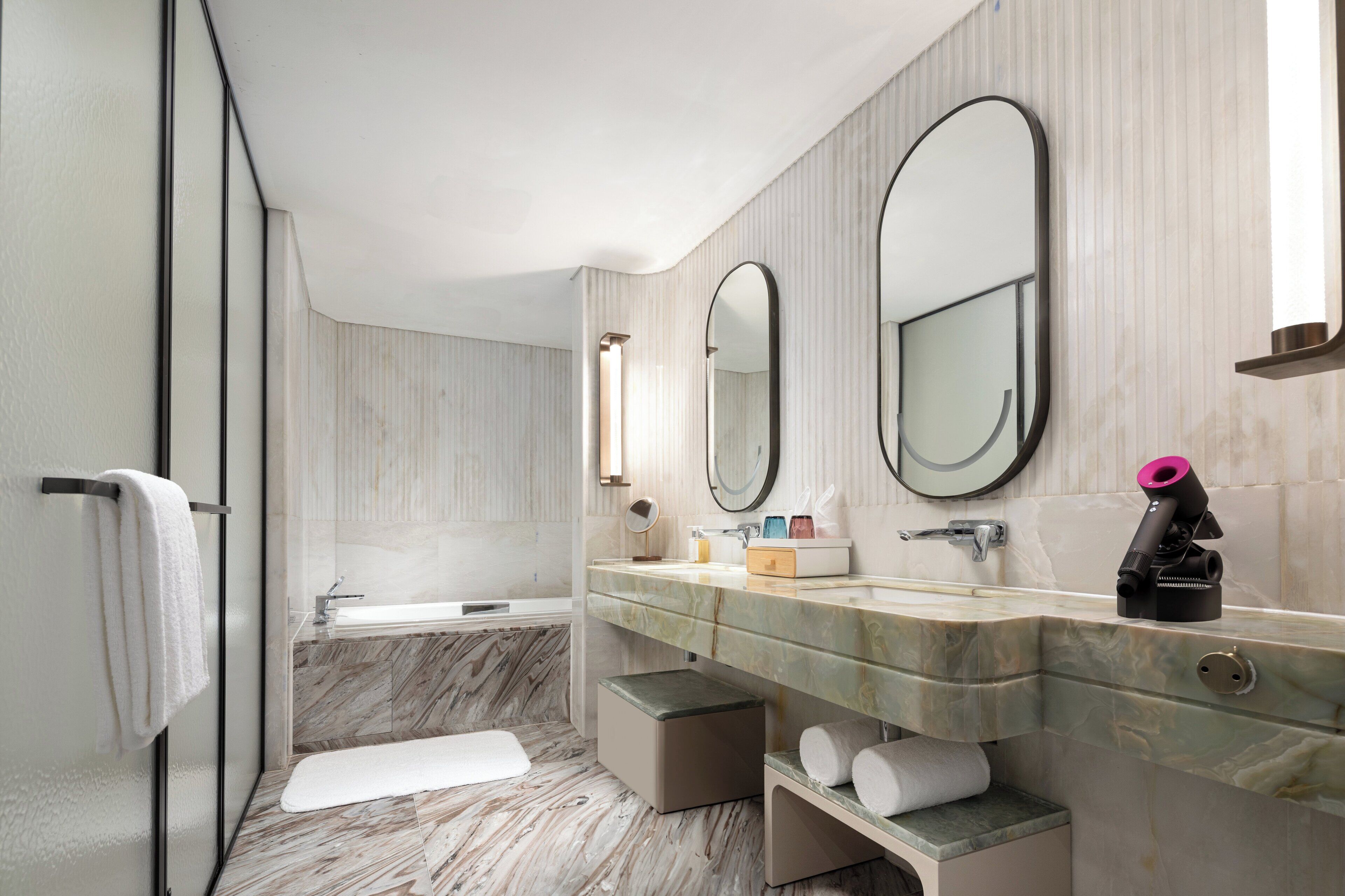A modern bathroom with a marble vanity, a bathtub, and a large mirror.