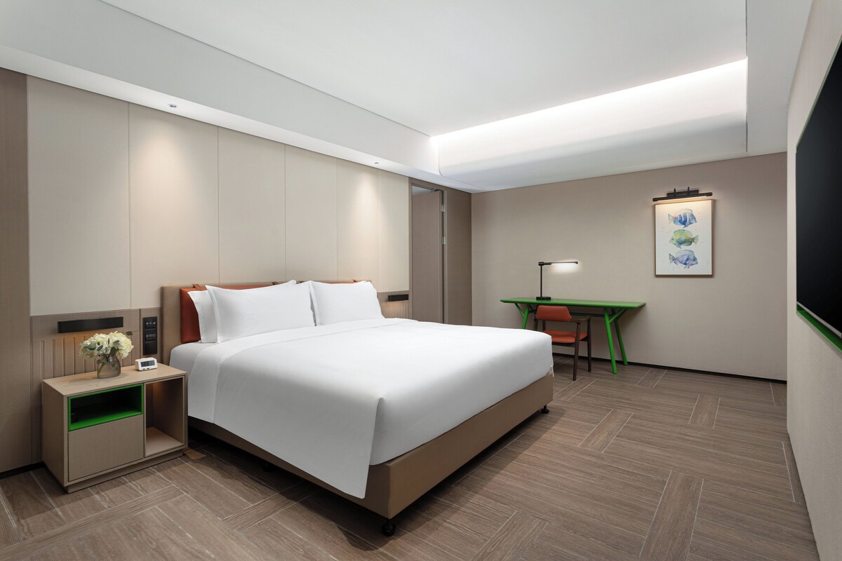 A modern hotel room with a large bed, a desk, and a nightstand.