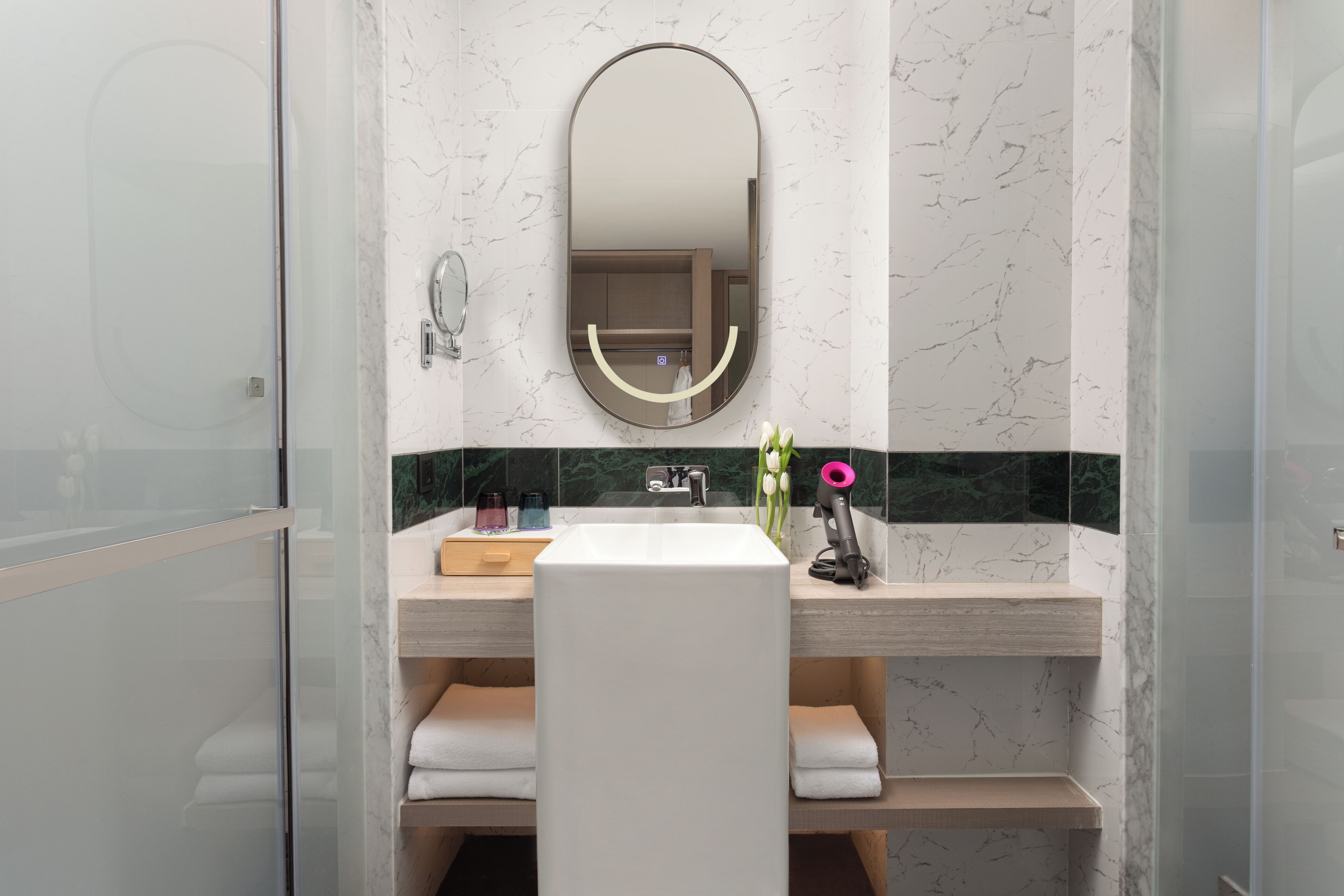 Un baño moderno con cabina de ducha de vidrio, lavamanos blanco y tocador con espejo.
