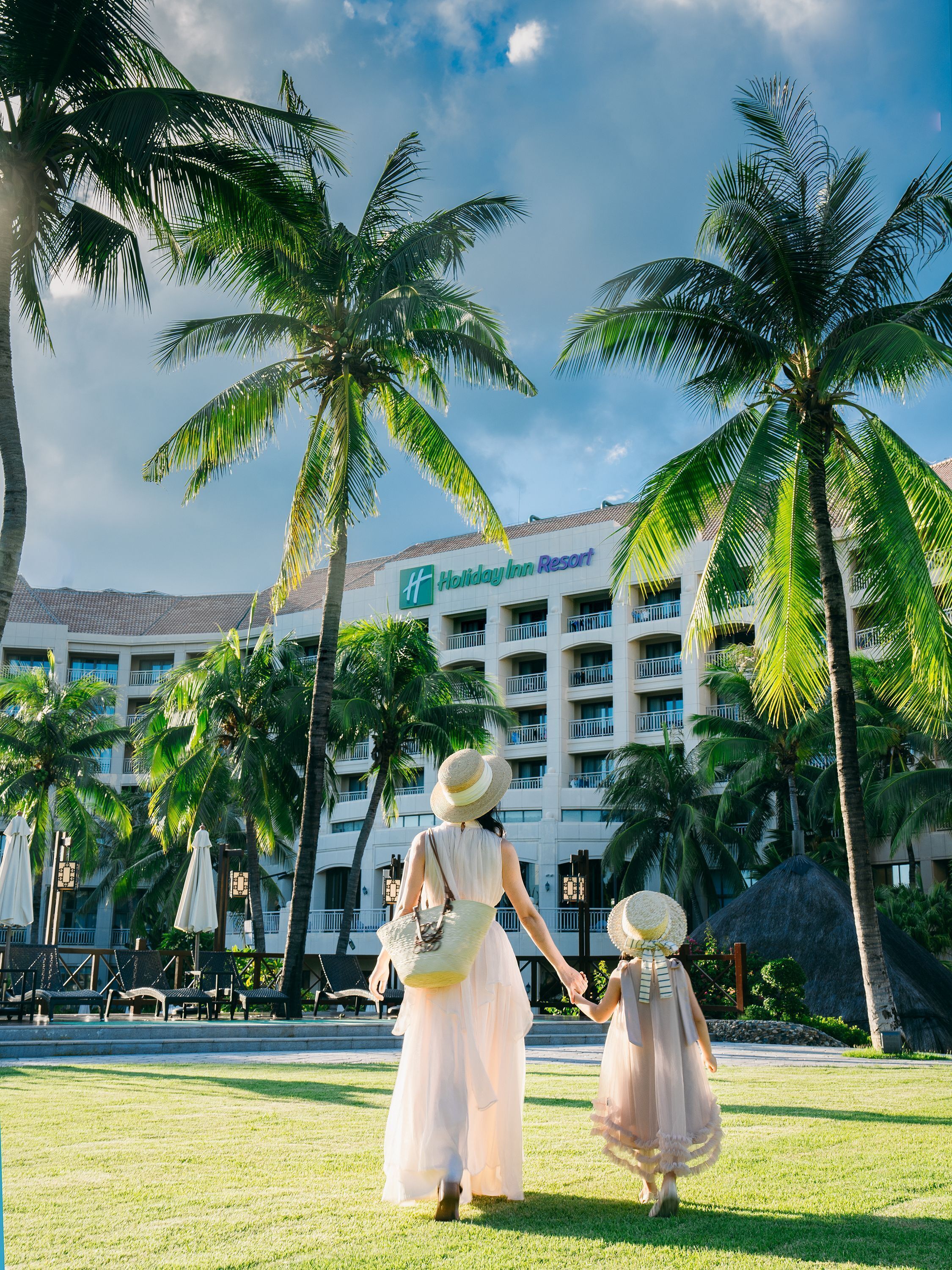 A Holiday Inn Resort with a large building, palm trees, and a grassy area.