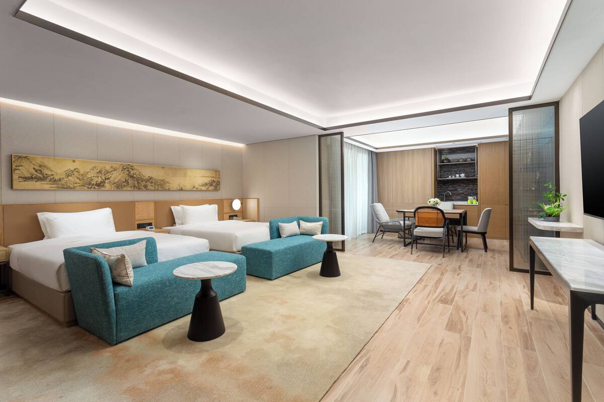 Ein modernes Hotelzimmer mit einem großen Bett, zwei Sofas, einem Essbereich und einer Küche im Hintergrund.