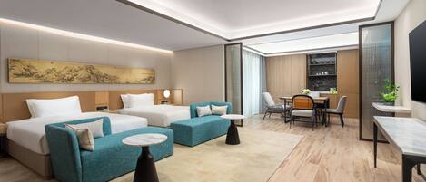A modern hotel room with a large bed, two sofas, a dining area, and a kitchen in the background.