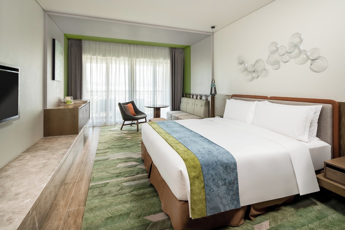 A hotel room with a large bed, a desk, a chair, and a TV.