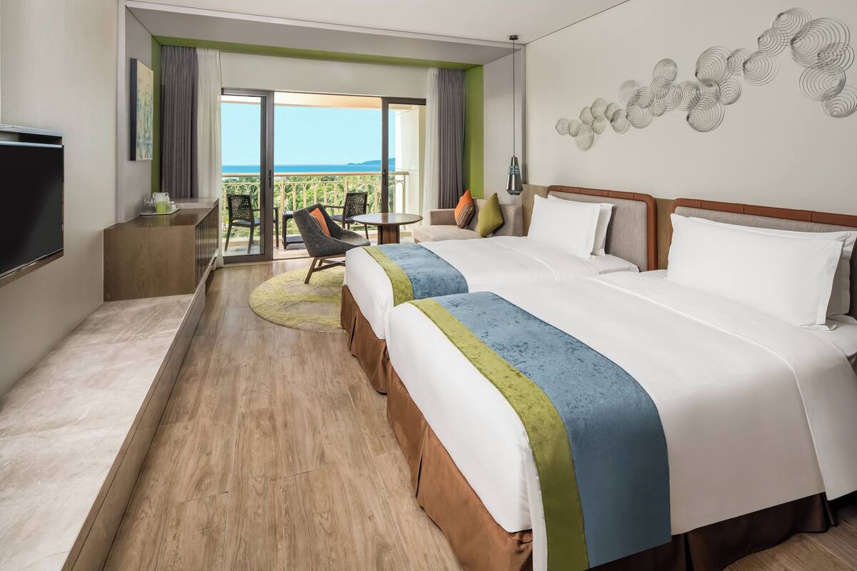 Ein Hotelzimmer mit einem großen Bett, einem Fernseher, einem Balkon mit Blick und einem Essbereich mit Tisch und Stühlen.