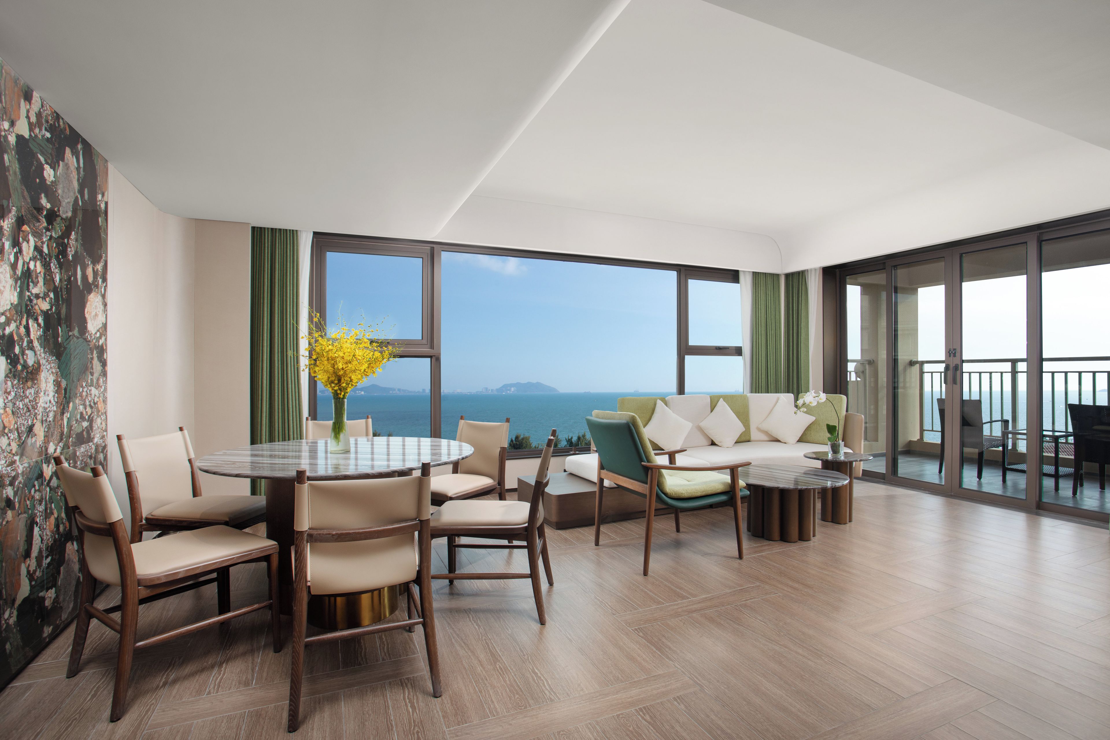 A modern interior with a dining area, seating, and large windows offering a view of the sea.