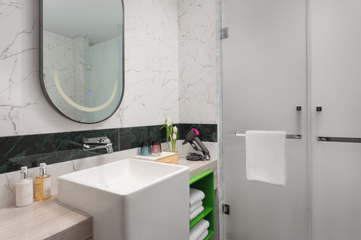 A modern bathroom with a large white bathtub, a green vanity, a mirror, and a towel rack.