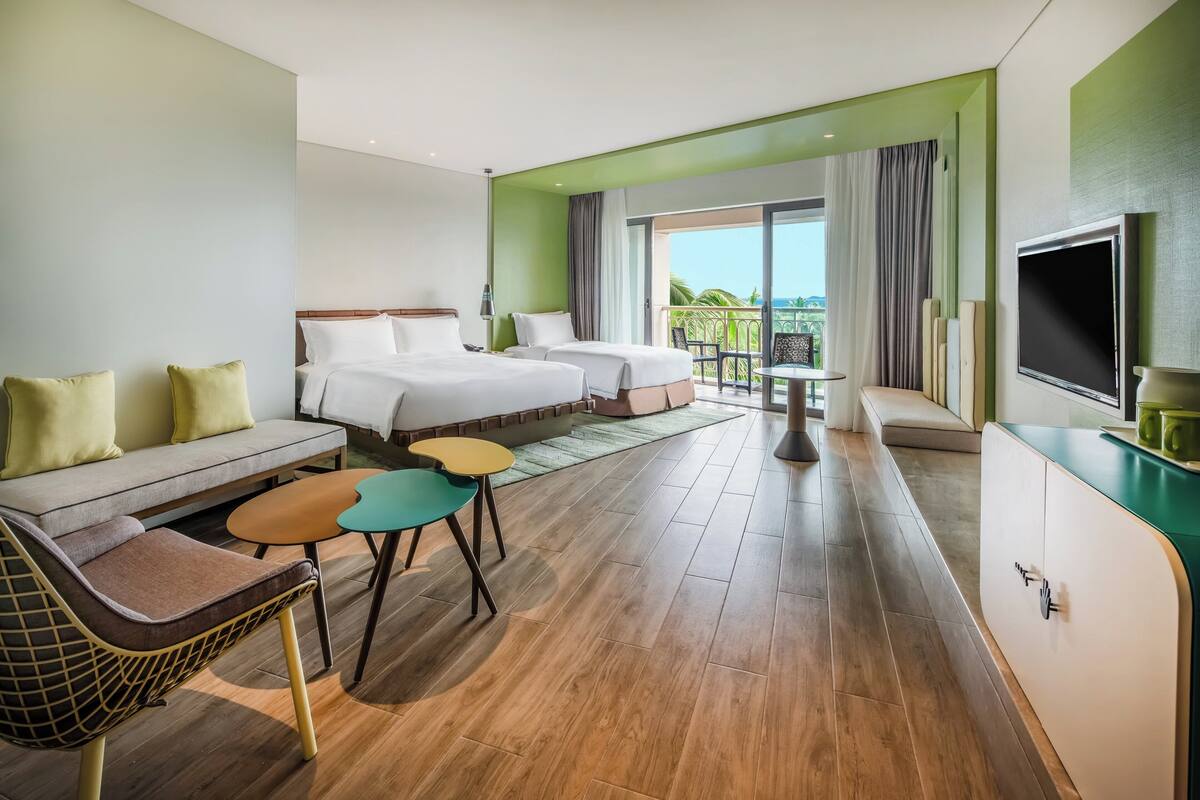 Ein Hotelzimmer mit zwei Betten, einer Sitzecke, einem Fernseher und einem Balkon mit Blick.