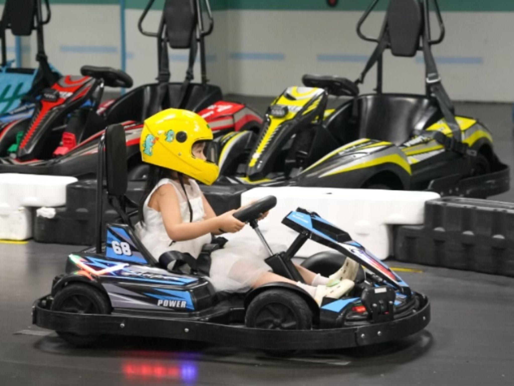 A go-kart track with a go-kart and a driver wearing a yellow helmet.