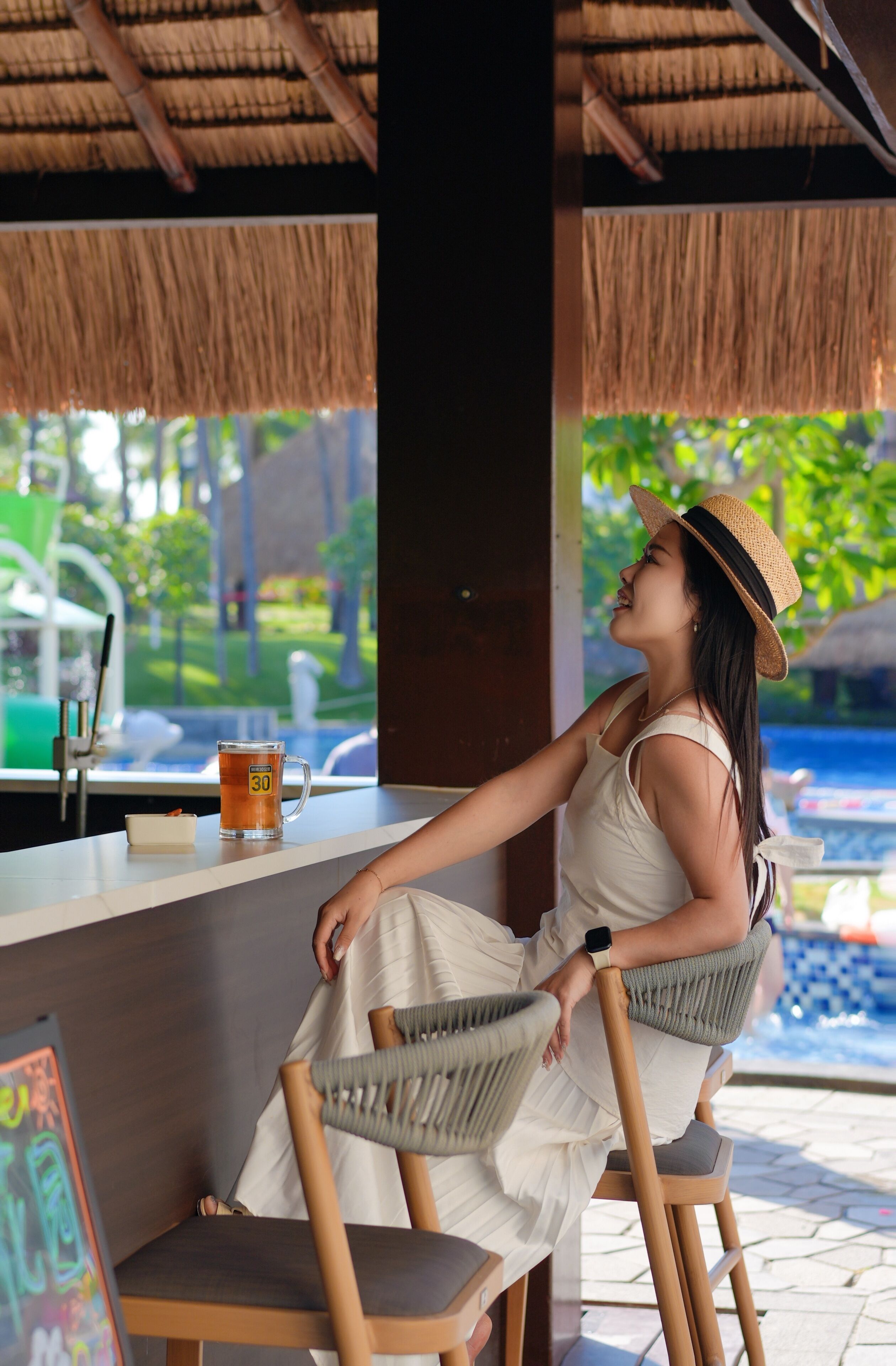 Une personne assise à une table, un verre à la main, avec vue sur une piscine.
