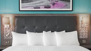 A hotel room with a large bed, a dark headboard, two bedside lamps, a framed picture of boats on a beach, and a nightstand with a lamp and outlet.