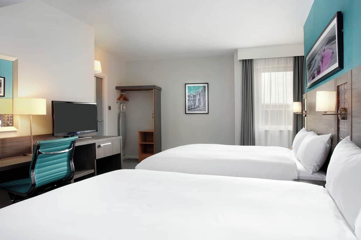 A hotel room with two beds, a desk with a TV, a chair, and a shower area.