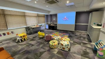 Children can play and relax in this vibrant playroom with a large screen, colorful chairs, and storage bins.
