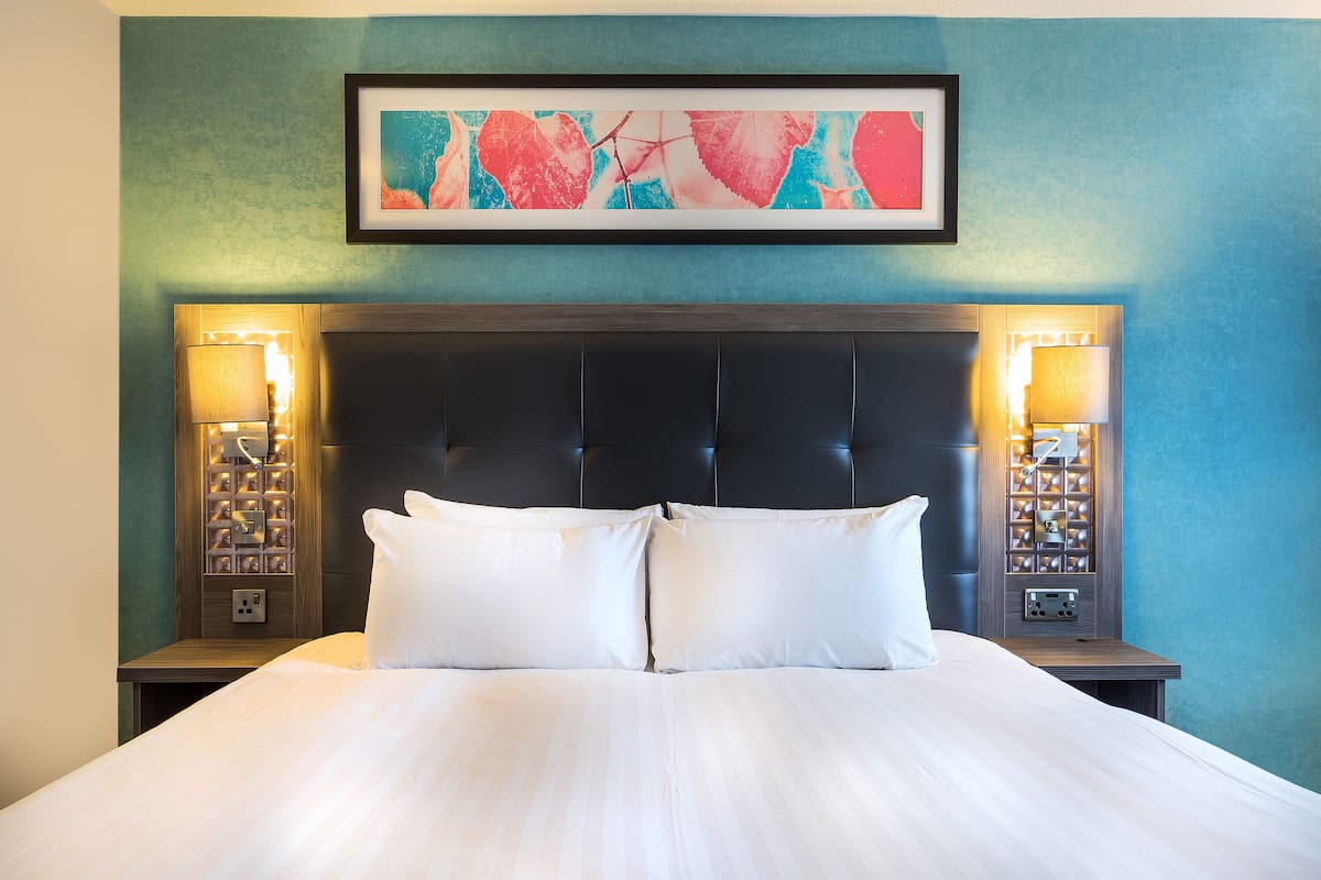 A neatly made bed with white linens, a dark headboard, and two bedside lamps.