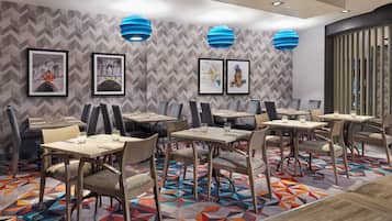 A modern dining area with geometric patterned wallpaper, blue pendant lights, and framed artwork on the walls.