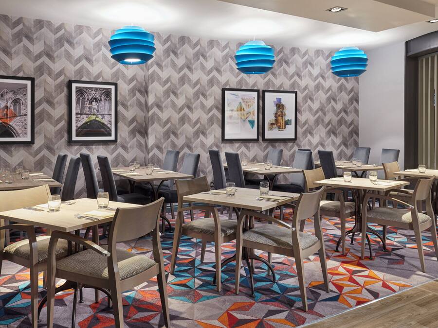 A modern dining area with geometric patterned wallpaper, blue pendant lights, and framed artwork on the walls.