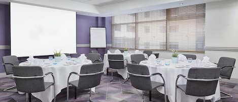 A conference room with multiple tables, chairs, a whiteboard, and a projector screen.