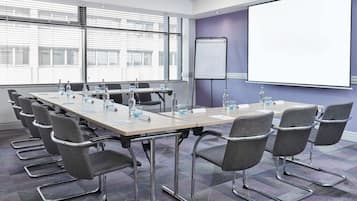 A conference room with a long table, chairs, a projector screen, and a whiteboard.