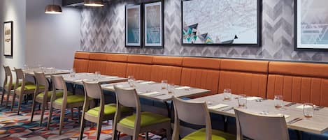 Un área de comedor con varias mesas y sillas, una alfombra estampada y un diseño de pared tipo espiga.