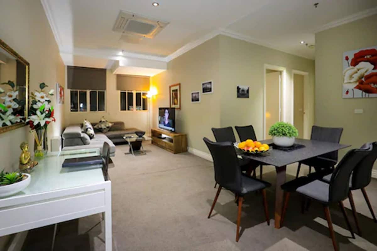 A dining area with a table set for four, a sofa, and a television in the background.