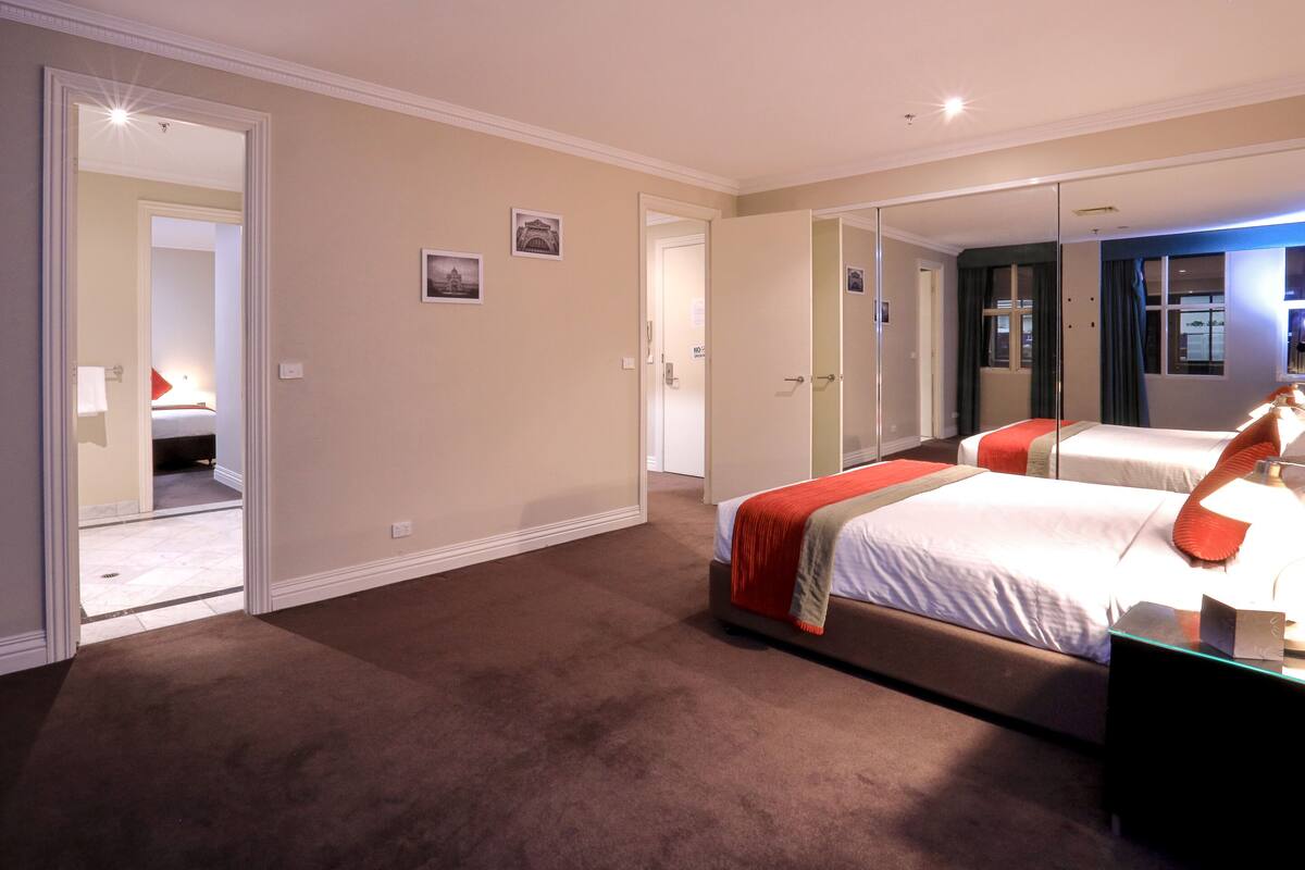 A hotel room with a large bed, a bedside table, a mirror, and a door leading to another room.