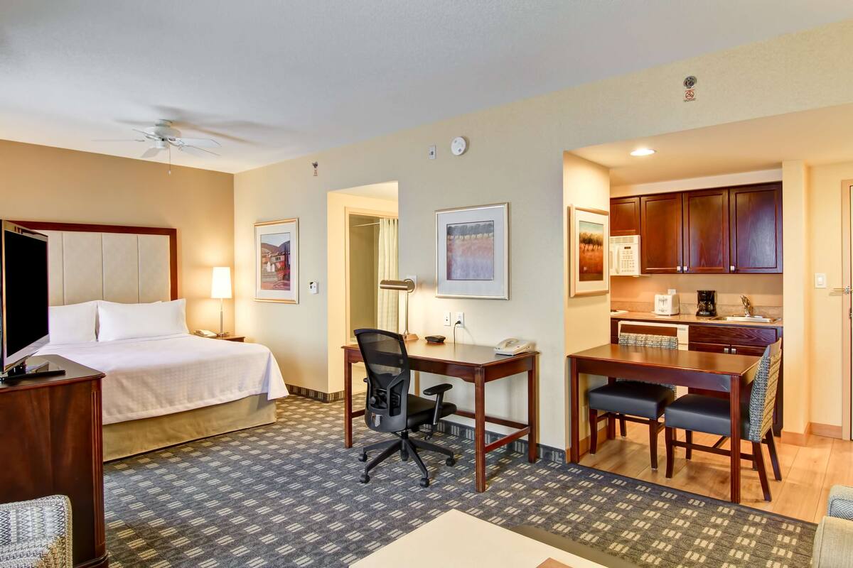 Habitación de hotel con cama, escritorio, silla de oficina, kitchenette y una mesa de comedor con sillas.