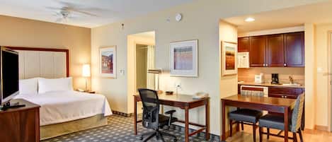 A hotel room with a bed, desk, office chair, kitchenette, and a dining table with chairs.