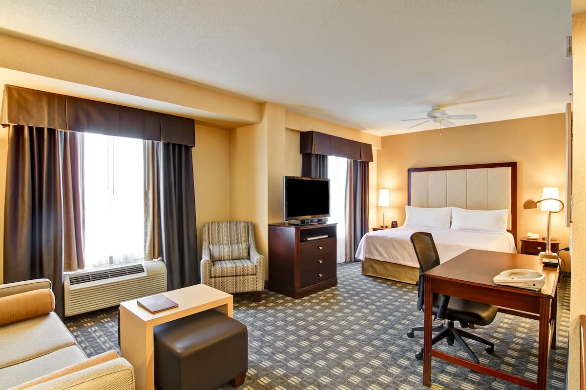 Habitación de hotel con cama, escritorio, silla, televisor y aire acondicionado.
