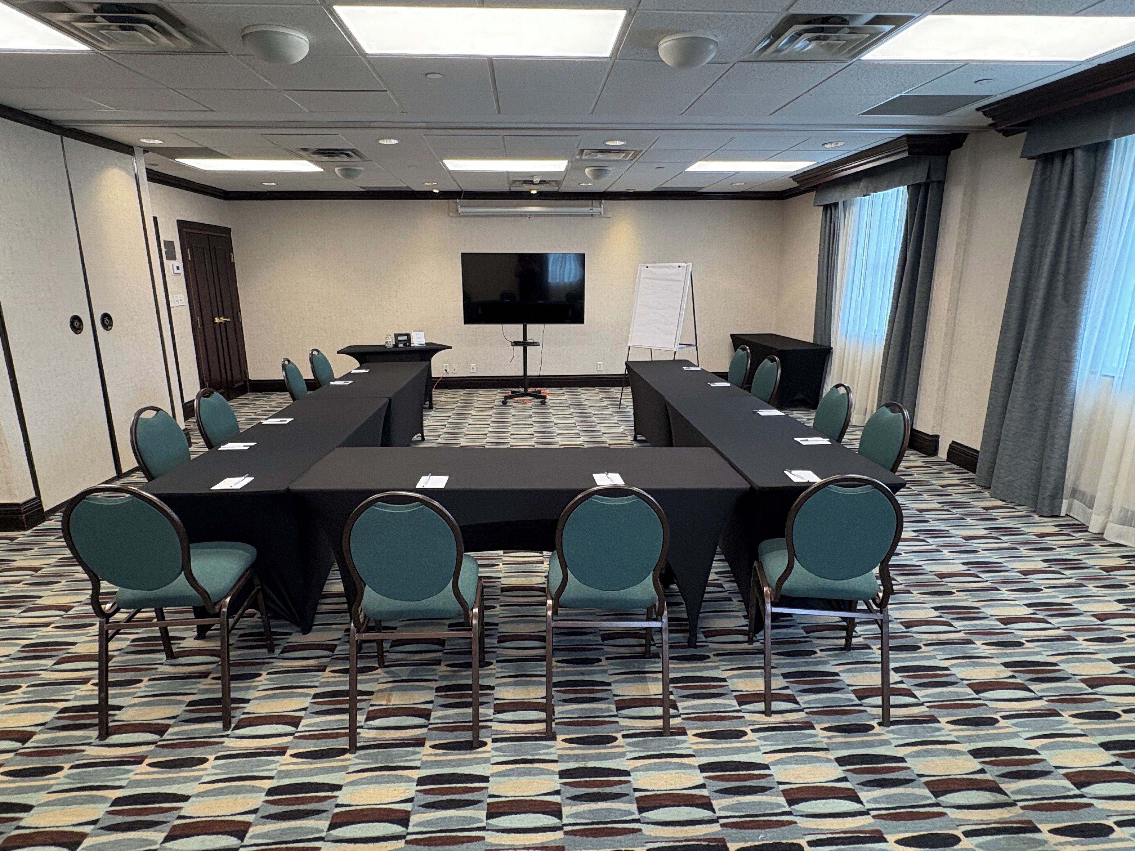 A conference room with a long table, chairs, a TV screen, and a whiteboard.