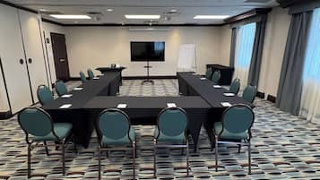 A conference room with a long table, chairs, a TV screen, and a whiteboard.