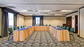 A conference room with a long table, green chairs, and a patterned carpet.