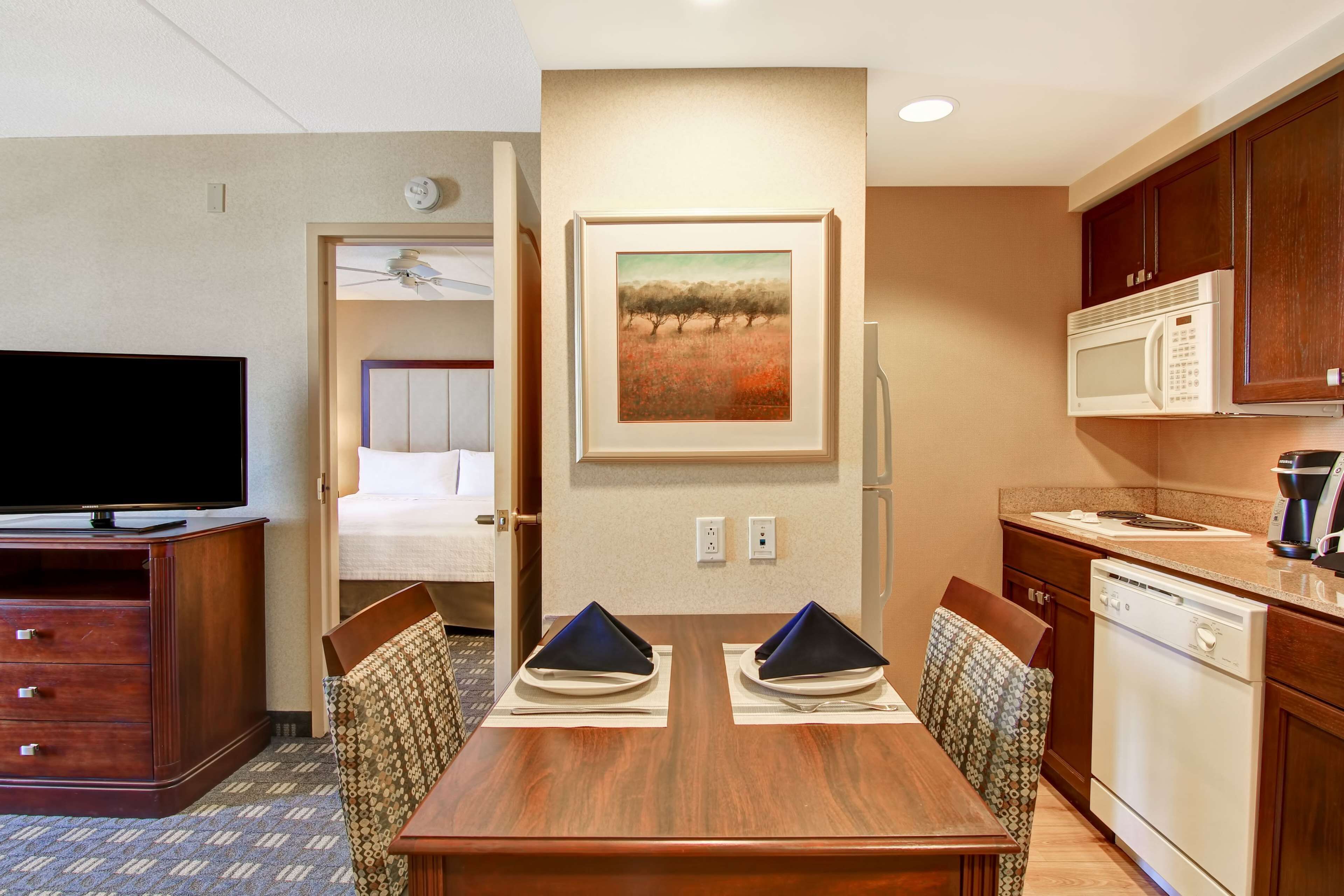 A hotel room with a dining area, a television, a microwave, and a painting on the wall.