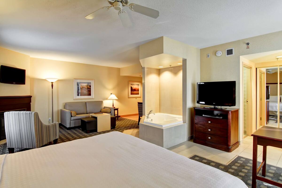 Habitación de hotel con una cama grande, un sofá, televisión, escritorio, silla, bañera y ventilador de techo.