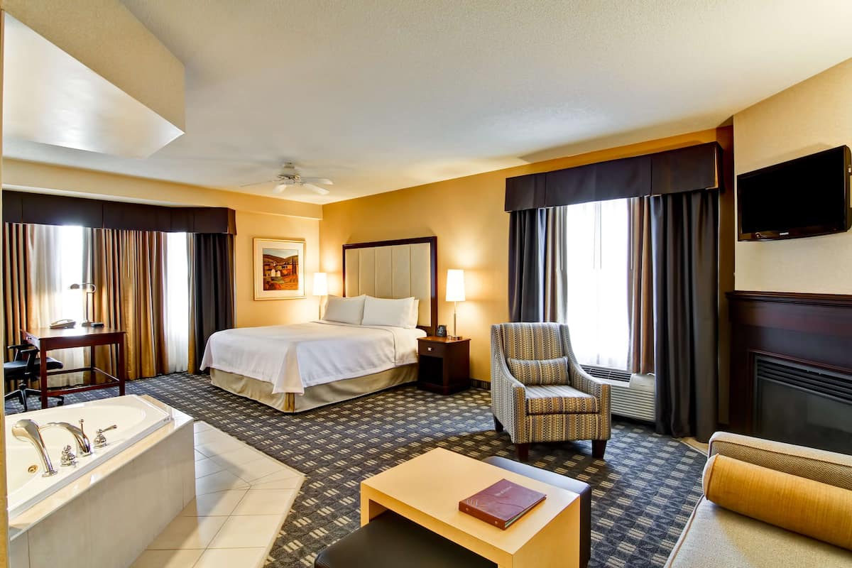 Habitación de hotel con cama, escritorio, silla, televisor, chimenea y baño con bañera.
