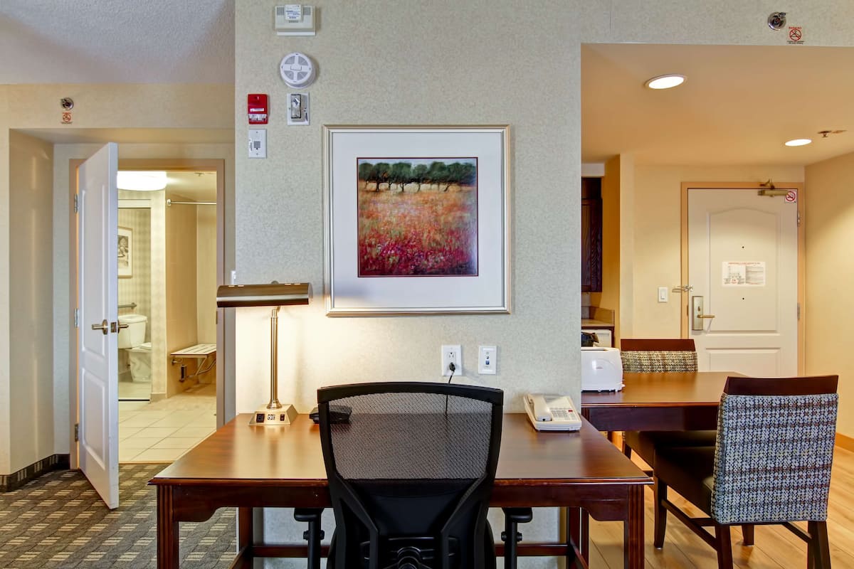 Habitación de hotel con comedor, un cuadro en la pared y una puerta que da al baño.