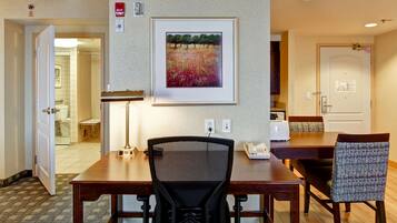 A hotel room with a dining area, a painting on the wall, and a door leading to a bathroom.