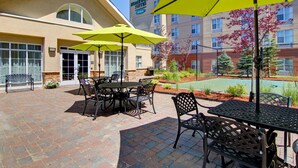 Une terrasse d’hôtel avec des espaces de repos en plein air, des parasols et un espace piscine.