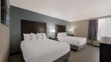A hotel room with two beds, a large painting on the wall, a desk, and a window with curtains.