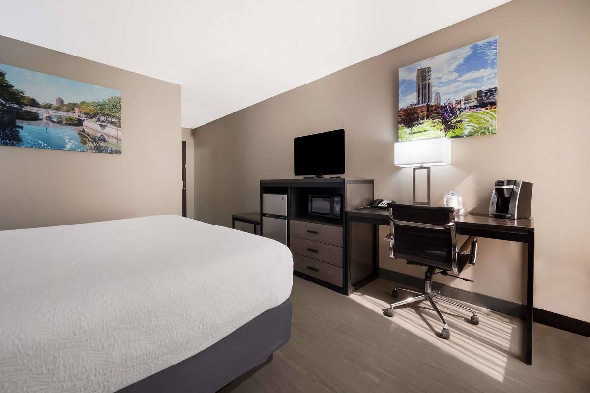 A hotel room with a bed, a desk with a computer, a TV, and two paintings on the walls.