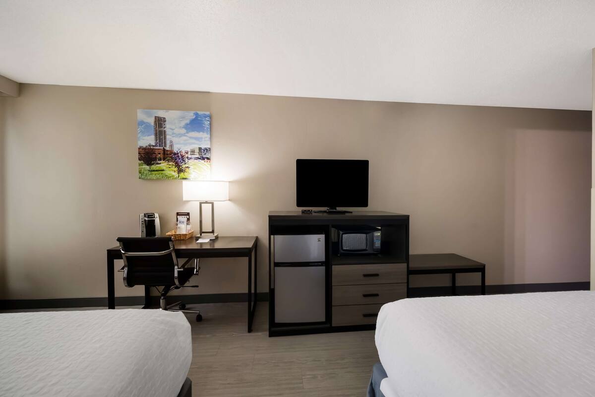 A hotel room with two beds, a desk with a chair, a television, a refrigerator, and a microwave.