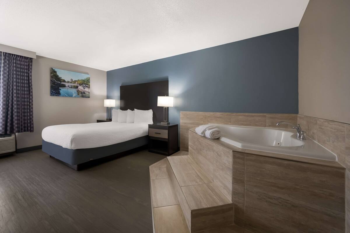 A modern hotel room with a large bed, a separate bathroom with a bathtub, and a painting on the wall.