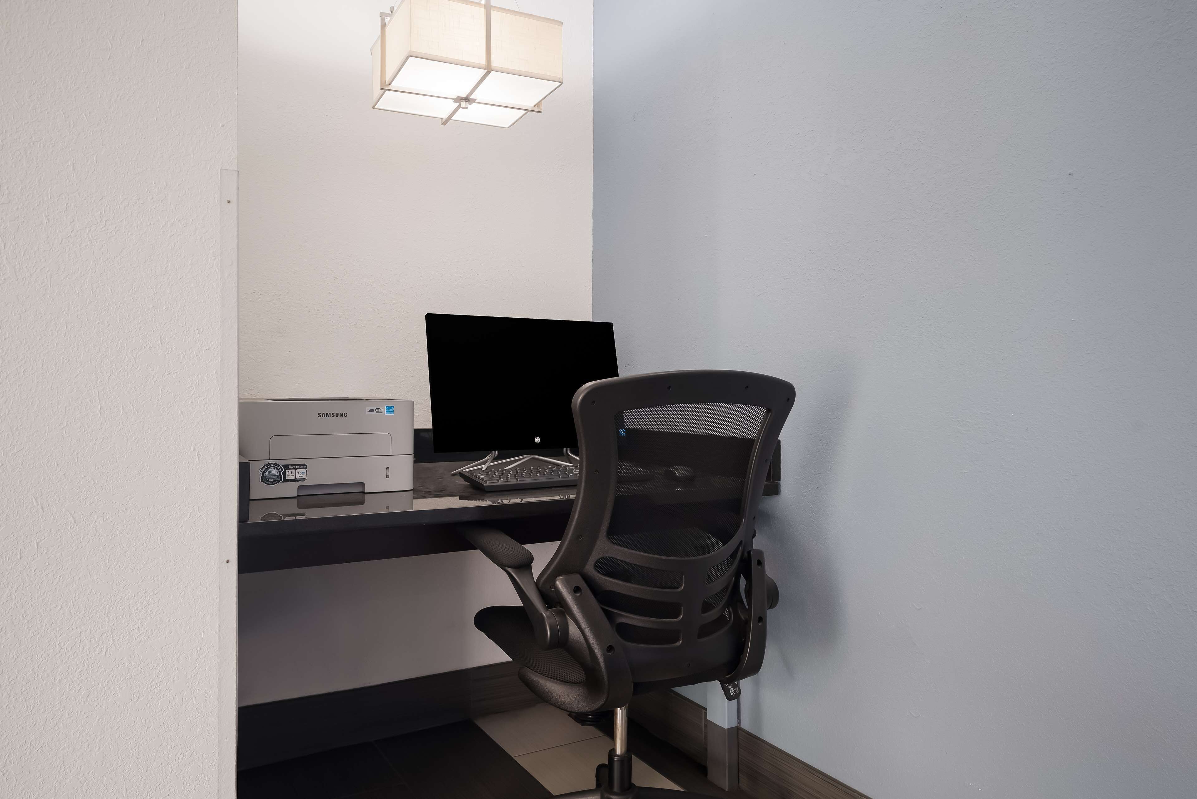 Un escritorio con una impresora, un monitor de computadora y una silla de oficina negra.