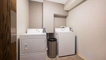 A laundry room with two stacked washers and dryers, a trash can, and a wooden door.