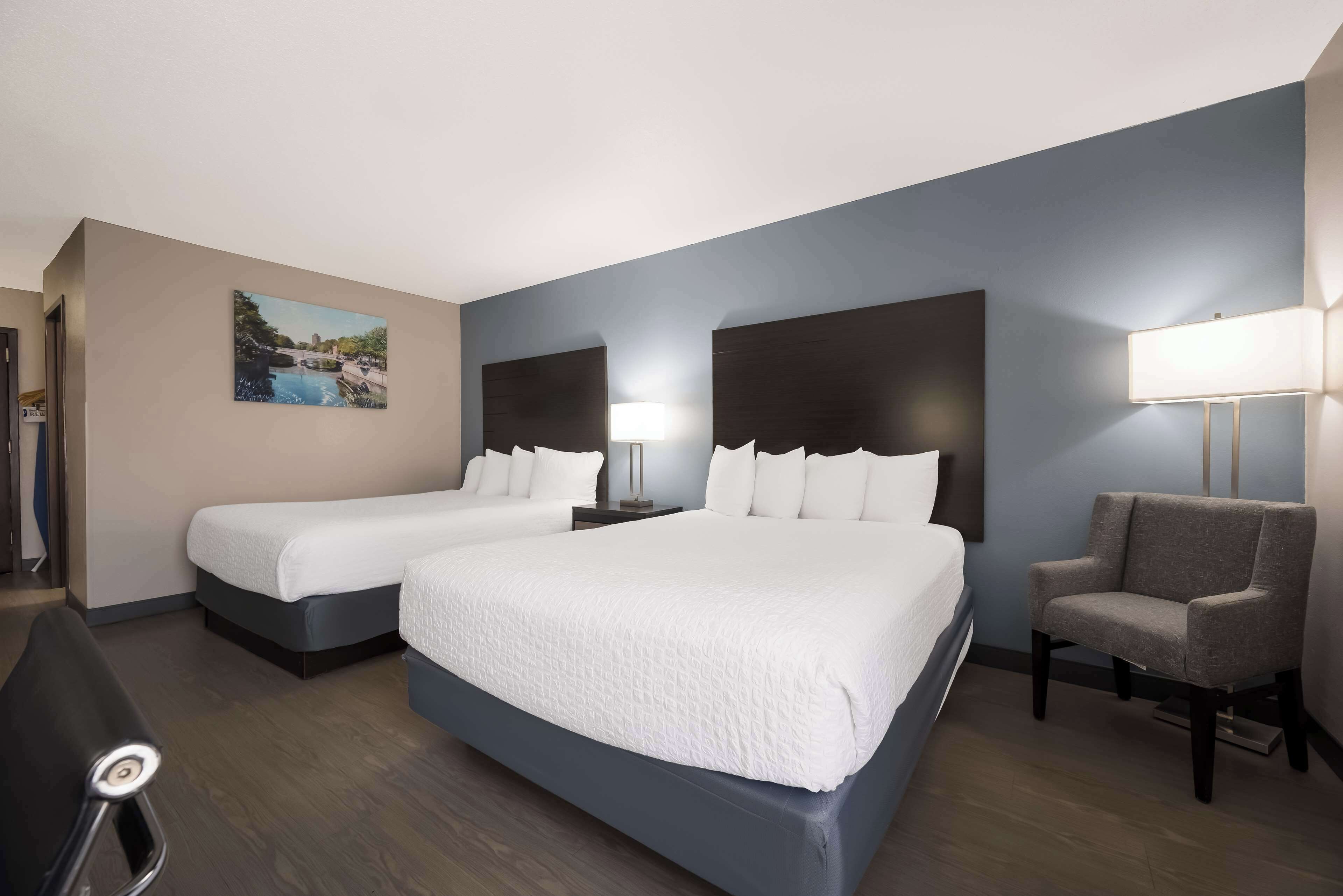 A hotel room with two beds, a desk, a chair, and a painting on the wall.