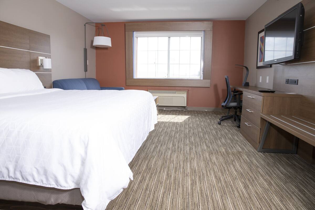 A hotel room with a large bed, a desk with a chair, a television, and a window with blinds.