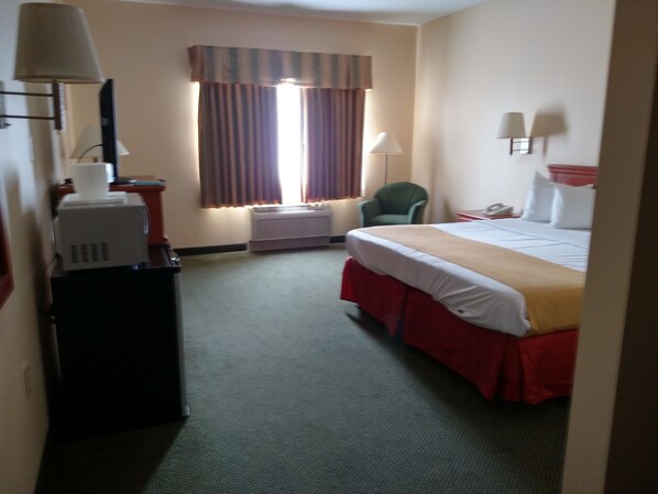A hotel room with a bed, a desk with a lamp, a chair, and a window with curtains.