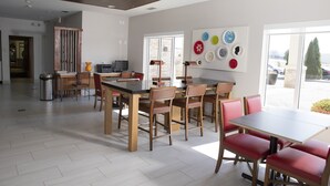A modern dining area with wooden tables and chairs, a large window with a view, and a wall decorated with plates. - Holiday Inn Express Toledo West - Napoleon by IHG (Napoleon)