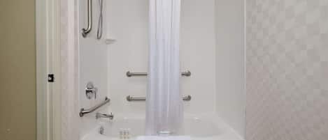 A bathroom with a white bathtub, a shower with grab bars, and a white curtain.
