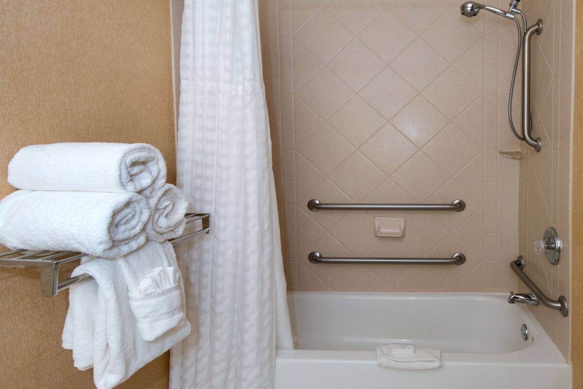 Een badkamer met een witte badkuip, een douche met handdouche en een handdoekrek met opgevouwen handdoeken.