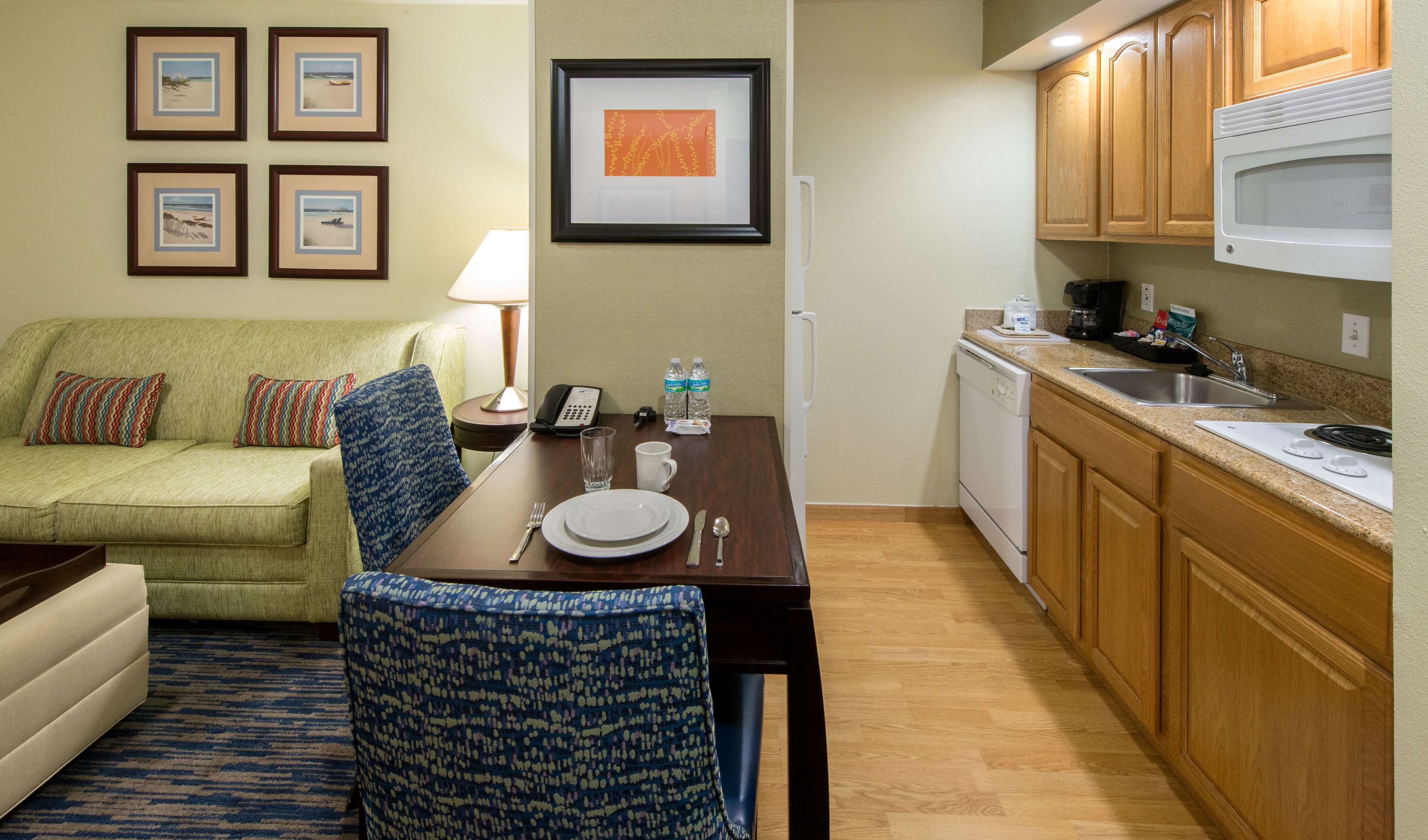A compact hotel room with a dining area, kitchenette, and a sofa with patterned cushions.