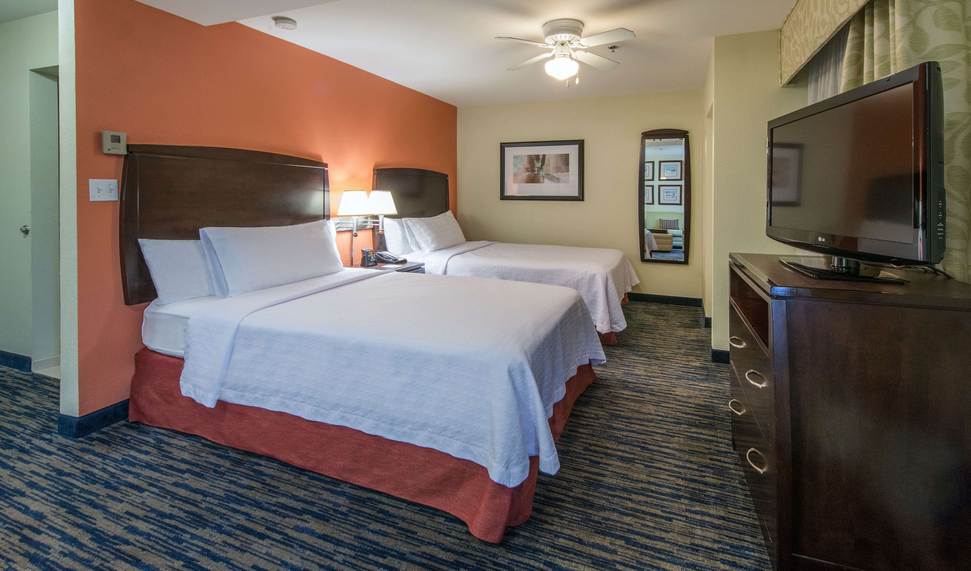 A hotel room with two beds, a television, a desk with a lamp, and a ceiling fan.